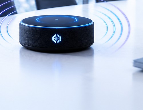 The NeMeets meeting speaker on a conference table, with a blue LED ring and sound waves radiating outward.
